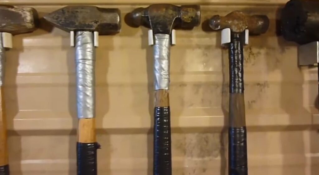 > Martelos pendurados em suporte feito com cano de PVC cortado em U, fixado em parede de oficina.

